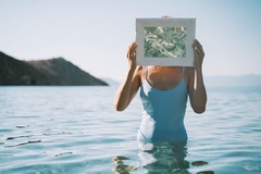 woman stands in sea, holding mirror in front of face