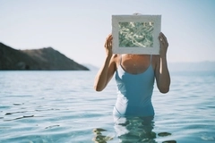 Image woman stands in sea, holding mirror in front of face