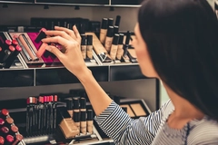 Image A woman grabbing a lip product out of a display.