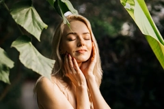 Image A woman touching her face in front of a leaf.