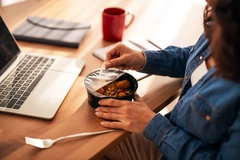Image A person eating an instant meal at their work desk.
