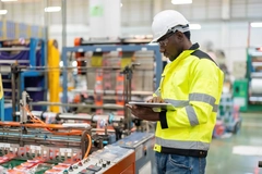male engineer standing in engine room Using a laptop to control a material production machine system