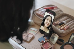 A woman putting on makeup and looking into a phone camera. 