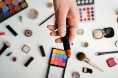 A woman's hand holding lipstick with other makeup in the background.