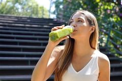 Healthy young woman drinking green smoothie detox juice outdoors.