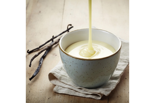 Image Vanilla sauce being poured into a ceramic bowl with vanilla beans on a rustic wooden table.