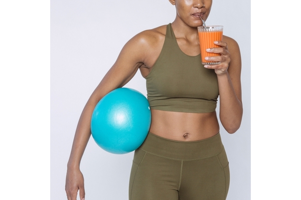 A woman in workout clothes drink a carrot smoothie.