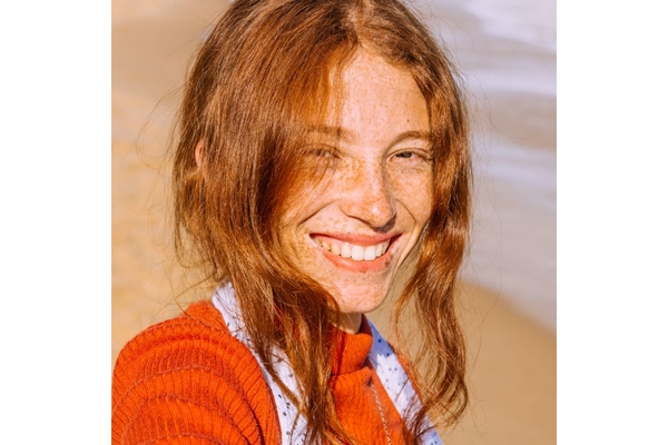 A smiling woman with freckles on her face looks directly at the camera.