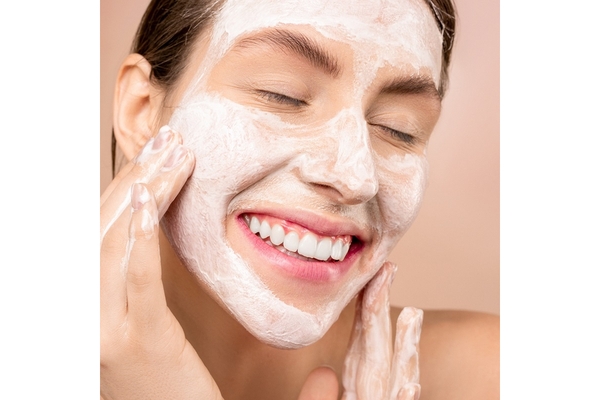 A woman smiles while applying a beauty mask to her face.