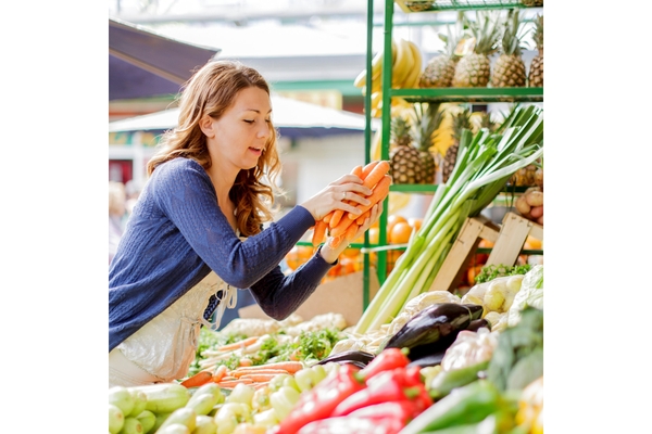 Image enthusiastic woman grabbing 3 carrots from a display outside.