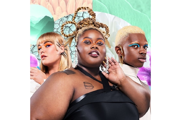Two women and a man wearing bright makeup strike a pose.