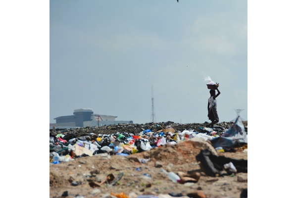 Image person carrying a bag on their head leaving a garbage dump