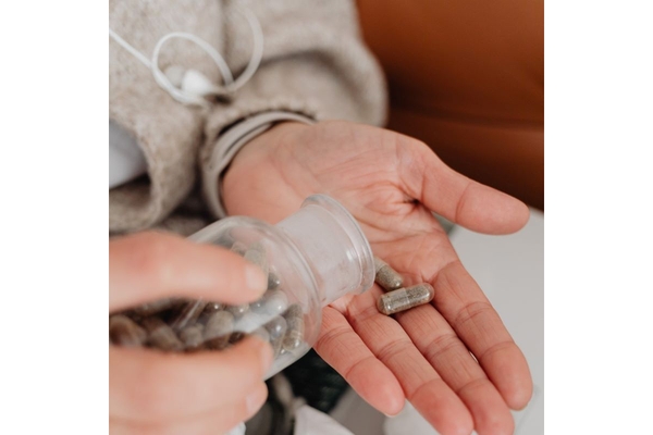 Person taking a supplement capsule out of a bottle.