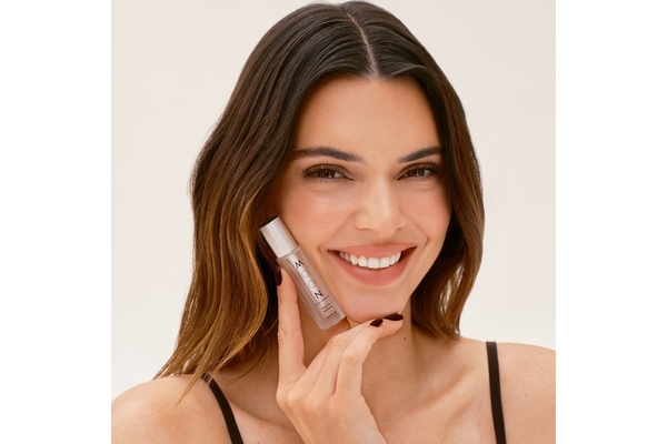 Image Model Kendal Jenner smiles while posing with a vial of Luminous Shine Teeth Serum by Moon Oral Beauty.