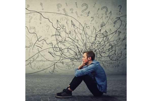 Man with mental health issues, sitting down with texts and question marks surrounding his head.