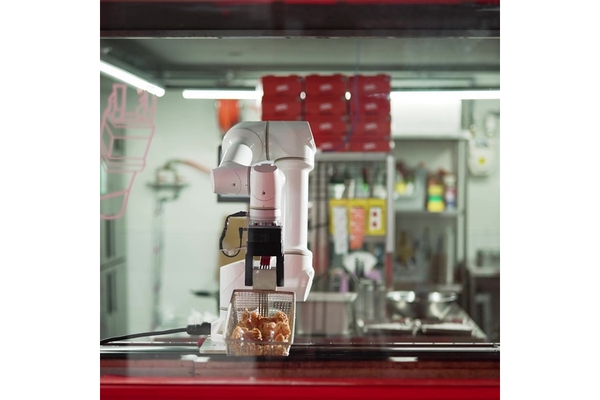 A robot cooking fried chicken on in a kitchen.