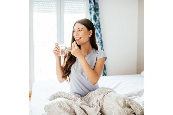 Image Woman taking a supplement while sitting in bed.