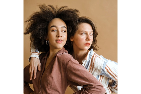 Two girls, one with curly afro and another with wavy hair with hands on hip pose looking to right.