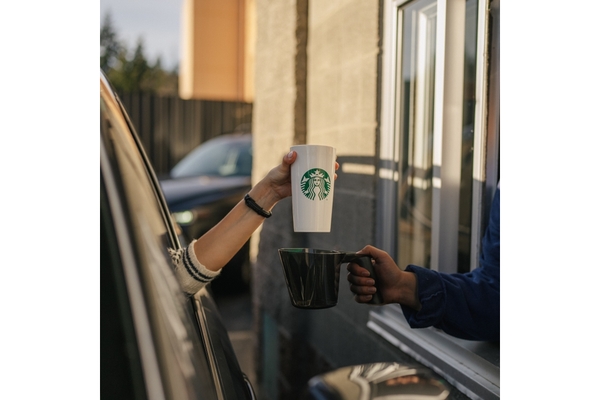 Image person in a car outside Starbucks collecting drive thru order at the pickup counter in reusable cup
