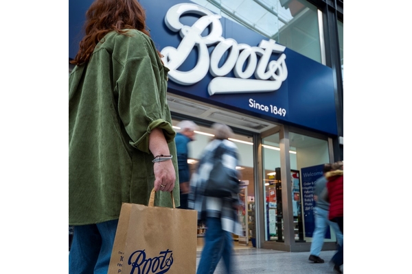 A woman holding a Boots bag in front of a Boots store.