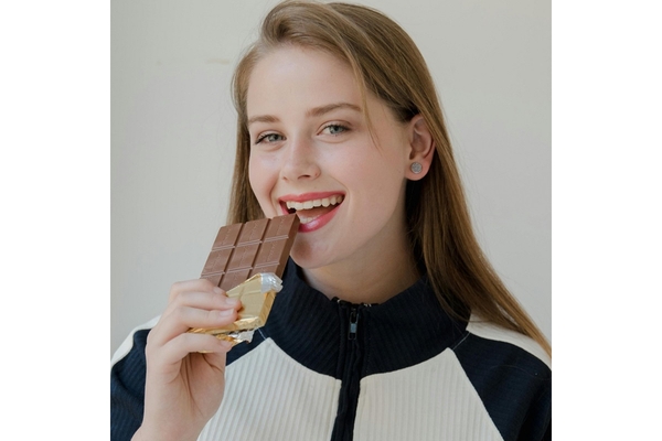 A girl smiling and holding a bar of chocolate in her hand close to the mouth.