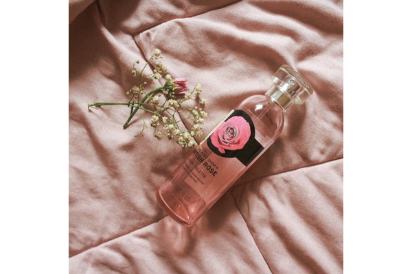 Image The Body Shop body spray laying on a pink bed sheet.