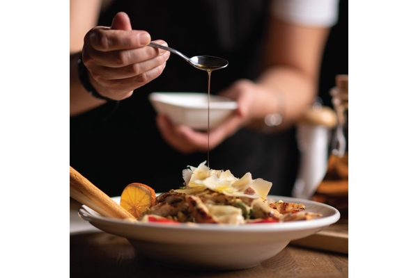 Image A hand pouring honey from a spoon into a bowl of salad.