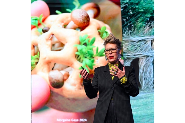 Image A woman with short hair and spectacles delivering a presentation on the stage.