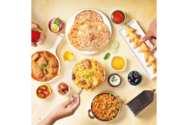 Image Biryani,mutton curry and samosas and two hands picking them up.