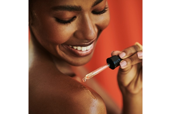 Image A woman smiling and putting a dropper of serum on her shoulder.