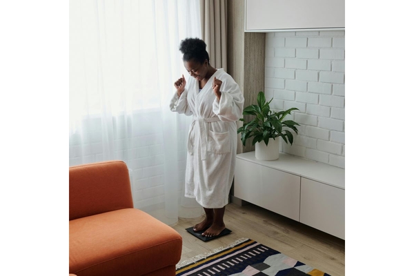Image Woman in a bathrobe, standing on a weight scale and looking happy.