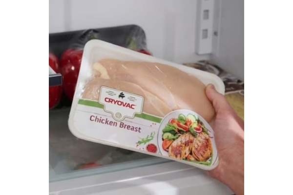 Hand holding chicken breast in wrapped food tray.