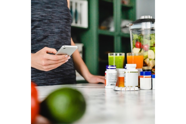Image Woman looks at phone, supplement bottles next to her.