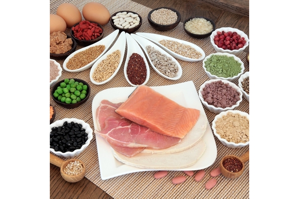 Image Sliced fish, nuts, protein powders, lentils, peas and eggs in white bowls kept on a wooden table.