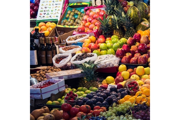 Image Fresh fruits, nuts, vegetables and olive oil displayed on a stand in an open air market.