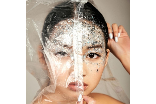 Image Woman wearing glitter makeup covers half her face with plastic