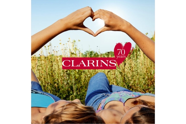 Two woman holding up heart hands while sitting in the grass.