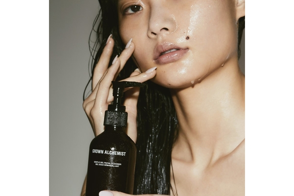 A woman with water on her face holding a Grown Alchemist product.