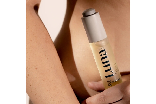 A hand holding a Luna Daily product in front of their leg.
