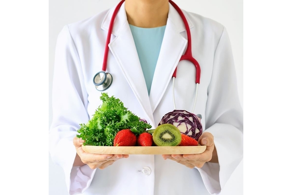 Person in a doctor's coat holding a plate of fruits and vegetables.
