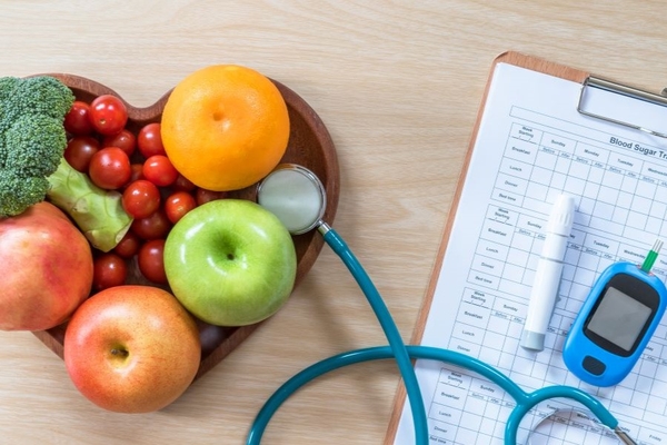 Image A diabetes test with a stethescope and a heart-shaped bowl of fruit on a table.