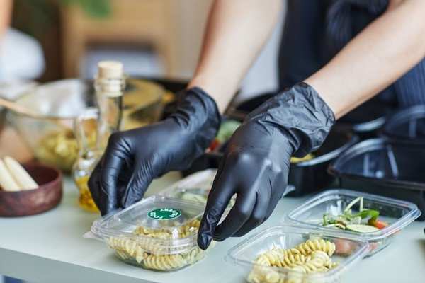 Image A person wearing black gloves holding a plastic container of pasta.