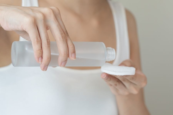 A person holding a bottle of makeup remover and a cotton pad.