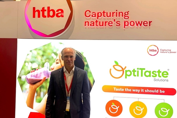 Image an old man in a suit standing in front of a digital signboard at a trade show