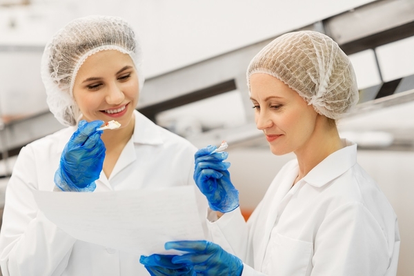 happy women technologists tasting ice cream in factory
