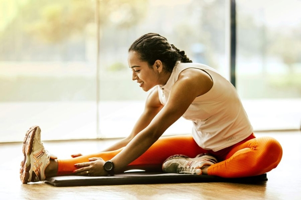 Image A woman stretches on a yoga mat in front of a large window overlooking a forest.