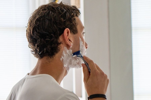 Image A man shaving his cheek.