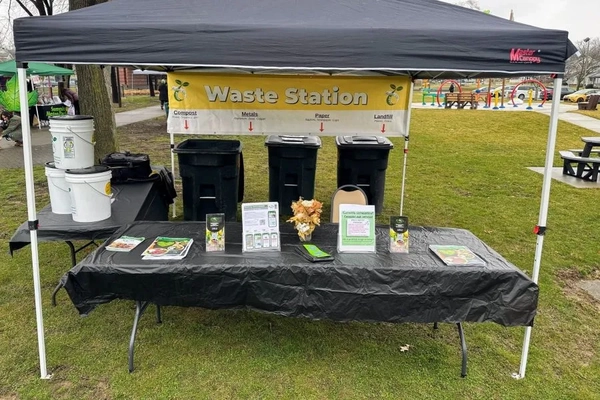 A black tent with a table with trash cans and a sign