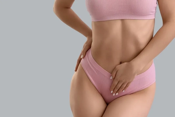 Image A woman wearing a pink underwear and bra set and putting her hand on her stomach.