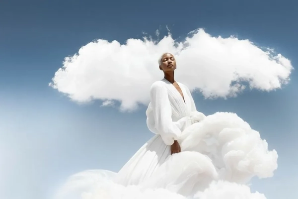 Image A woman wearing a white dress with clouds all behind her.